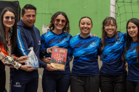 Cuatro integrantes del equipo femenino de fútbol sala posan junto al trofeo, el director de deportes y la jefe de la Oficina de Egresados